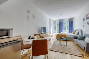 A modern, well-lit room with a dining table, chairs, a sofa, a bed, a TV, and a microwave. - New, Large and Cosy Studio - Le Marais - Mid Terms (Paris)