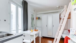 Kompakti keittiö, jossa on ruokapöytä, valkoiset kaapit ja tikkaat.