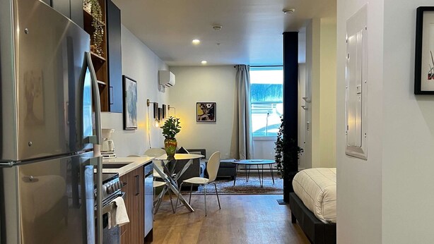 Una cucina moderna con elettrodomestici in acciaio inossidabile, una zona pranzo con tavolo e sedie, e una camera da letto con un letto.