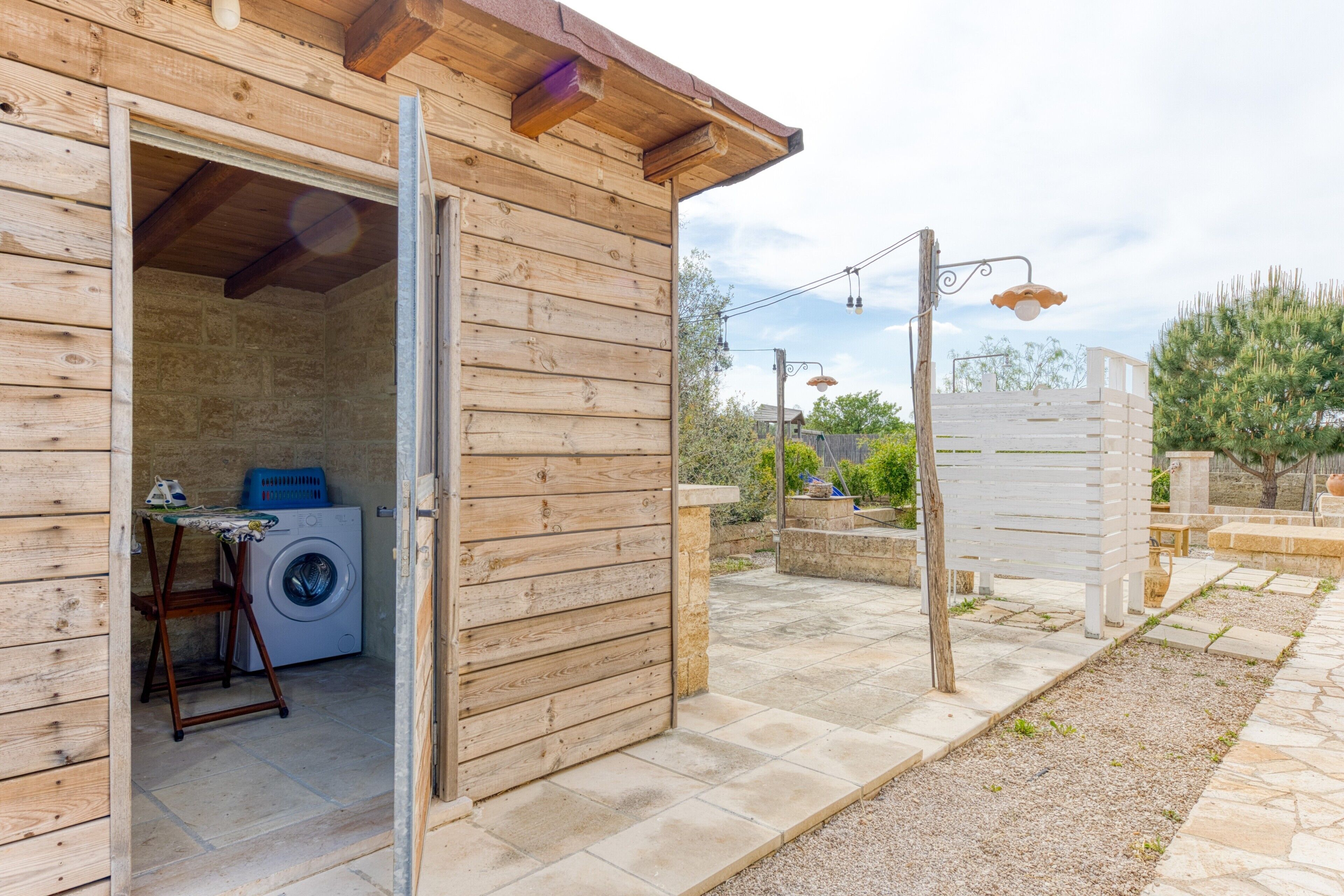 Un edificio in legno con una porta aperta, una lavatrice all'interno e un patio in pietra all'esterno.