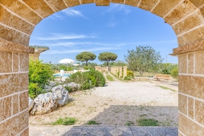 An arched stone structure leading to a landscaped area with trees and a pool.