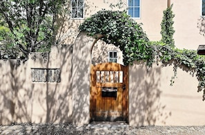A wooden door with a mailbox, a concrete wall, and a tree with green leaves. - Casa Alto - Well-appointed, fully furnished condominium in downtown Santa Fe. (Santa Fe)