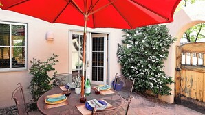 Eine Terrasse mit einem runden Tisch, Stühlen, einem roten Sonnenschirm und einem Holztor.