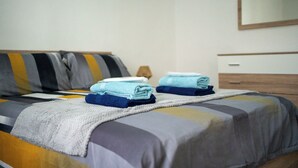 Cama bem arrumada com travesseiro listrado, toalha dobrada e mesa de cabeceira com abajur.