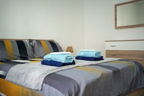 Ein ordentlich bezogenes Bett mit einem gestreiften Kissen, einem gefalteten Handtuch und einem Nachttisch mit einer Lampe.