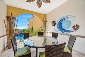 A round glass table with wicker chairs, a view of a pool, and a mural with a blue swirl and turtle. - Sunrise Tamarindo 22 (Tamarindo)