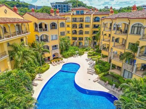 Um hotel com piscina central rodeada por vegetação exuberante e várias varandas.