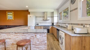 Une cuisine dotée d’un plan de travail en granit, de meubles en bois, d’un four encastré, d’un four à micro-ondes, d’un lave-linge et d’une machine à café.