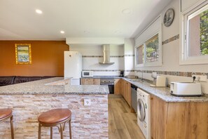 A kitchen with a granite countertop, wooden cabinets, a built-in oven, a microwave, a washing machine, and a coffee maker. - Villa 'Santa Susanna 18' with Sea Views (Santa Susanna)