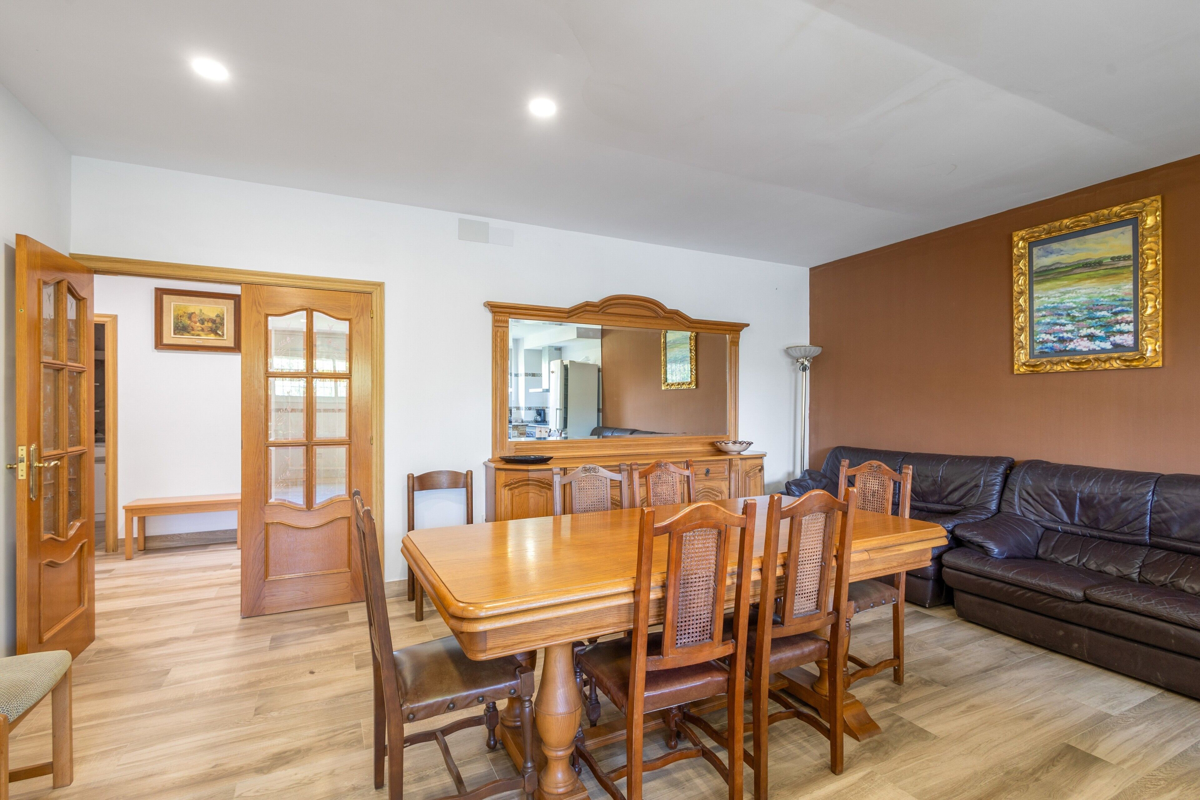 Un comedor con una mesa y sillas de madera, un sofá y un espejo sobre la mesa.