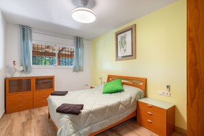 Une chambre à coucher comprenant un lit, une commode, une table de chevet, une fenêtre avec des rideaux et un luminaire au plafond.