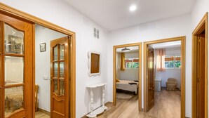 Un couloir avec des portes en bois, une console blanche et un lit à l’arrière-plan.