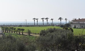 A coastal view with a fence, palm trees, and a building. - Magnificent villa in Santa Susanna, 100m from the beach, with pool and privacy (Santa Susanna)