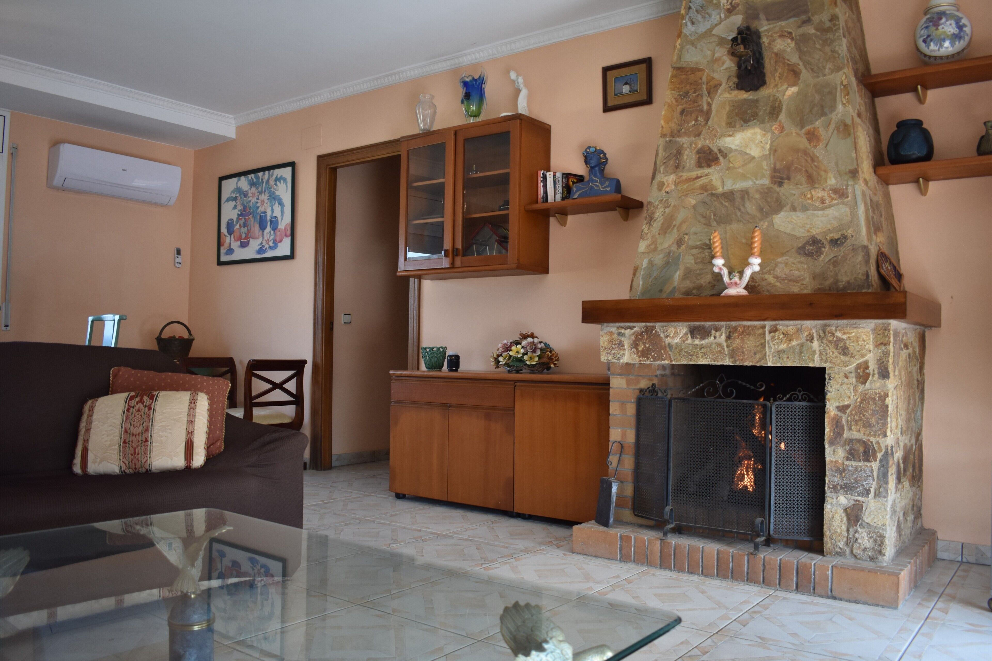 A living room with a fireplace, a glass coffee table, a sofa, and a wooden cabinet.