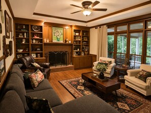 Ein Wohnzimmer mit Kamin, Bücherregalen, einer Couch und Blick durch große Fenster.
