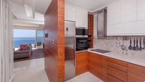 Cozinha moderna com uma geladeira grande, forno e micro-ondas. Há uma área de jantar com vista para o mar.