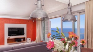 Uma sala de estar moderna com uma televisão grande, sofá cinzento e uma mesa com flores.