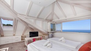 Quarto com uma janela grande, televisão, escrivaninha e duas camas.