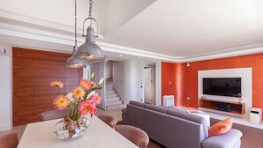 Uma sala de estar moderna com um sofá, uma mesa de jantar com flores, uma televisão e uma escada.