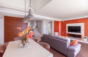 A modern living room with a sofa, a dining table with flowers, a TV, and a staircase. - Hedera Estate, Hedera A55 (Dubrovnik)