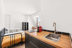 Ein kompaktes Studioapartment mit Bett, Küchenzeile und Blick auf die Stadt.
