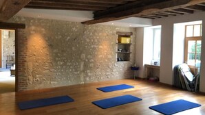 Una habitación con pared de piedra, vigas de madera y una ventana. Hay felpudos azules en el suelo.