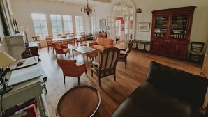 Un salón amplio con suelos de madera, una araña de cristal, un piano y un mueble grande con puertas de vidrio.