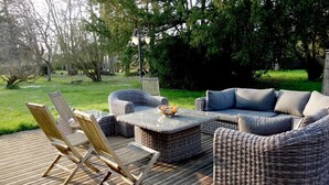 Una terraza con mobiliario de mimbre, incluyendo sillas y un sofá, además de una mesa con un cuenco de fruta.