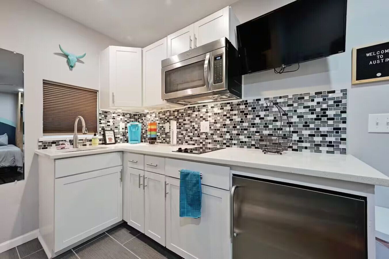 A modern kitchen with white cabinetry, a stainless steel microwave, and a tiled backsplash.