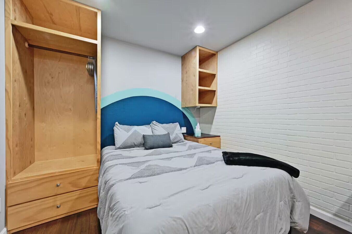 A bedroom with a bed, wooden wardrobe, and a nightstand.