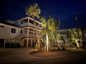 Un edificio de varios pisos con balcón, palmeras y un camino de entrada bien iluminado.