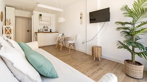 Un salon moderne comprenant un canapé, une table à manger avec des chaises, un téléviseur fixé au mur et une grande plante en pot.