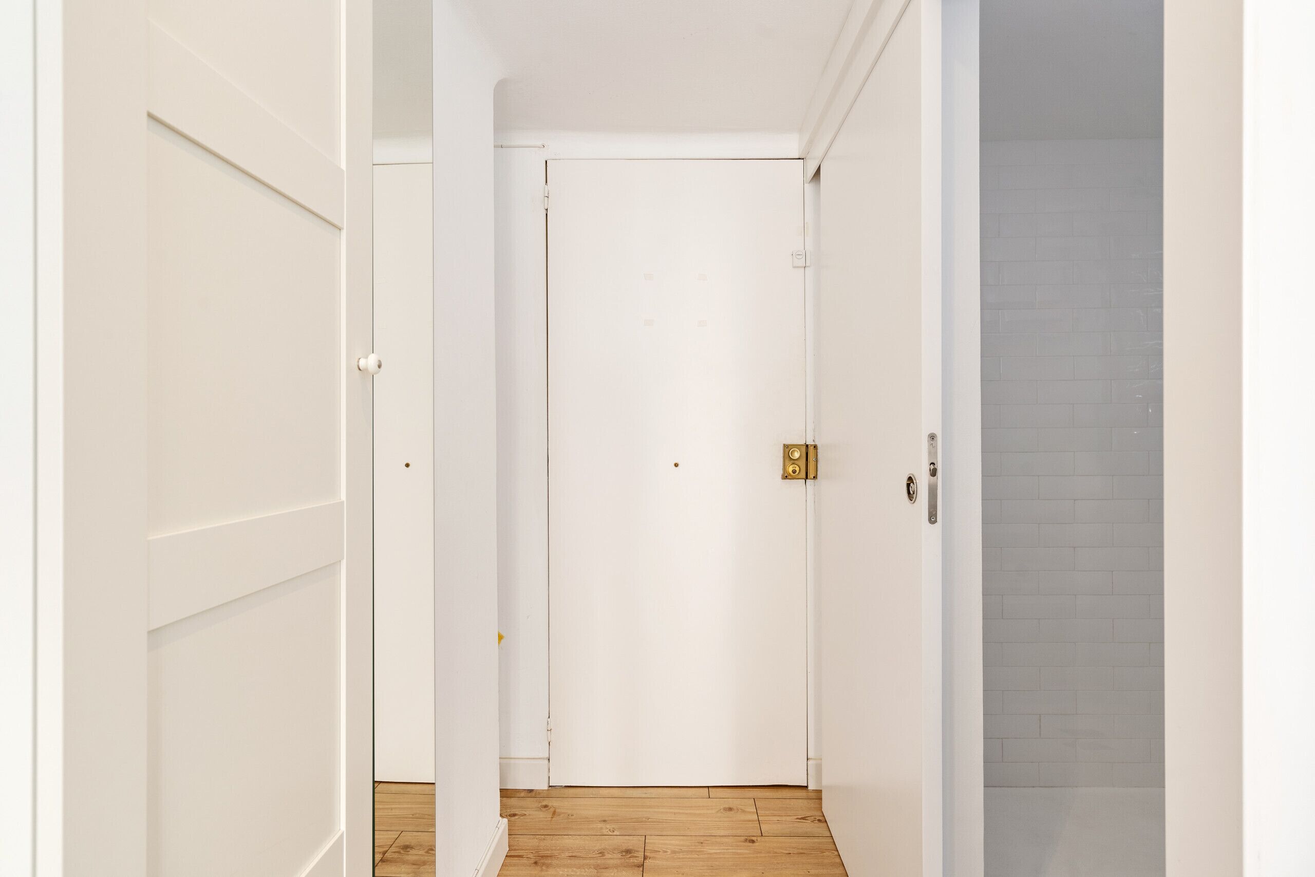 Un couloir étroit avec des portes blanches, un plancher en bois et un mur recouvert de carreaux.