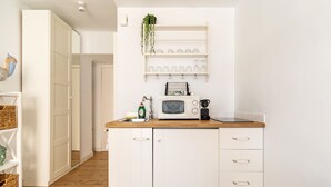 Une cuisine de taille réduite avec des meubles blancs, un four à micro-ondes, un évier et une plante suspendue.