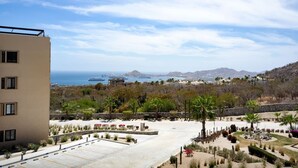 A building with a parking area, landscaped garden, and a view of the sea and mountains. - Condo with Arco views, infinity pool, and spa (Cabo San Lucas)
