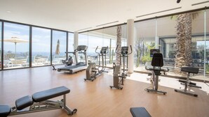 A spacious gym with cardio machines, a bench, and large windows offering a view of the outdoors. - Condo with Arco views, infinity pool, and spa (Cabo San Lucas)