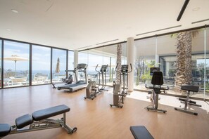 Een ruime fitnessruimte met cardioapparatuur, een bank en grote ramen met uitzicht op het omliggende landschap.