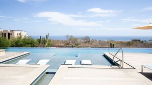 A pool with clear blue water, a view of the ocean, and a desert landscape in the background. - Condo with Arco views, infinity pool, and spa (Cabo San Lucas)