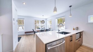A modern kitchen with a large island, stainless steel appliances, and pendant lighting. - Spa & Nature Escape | Le Nova (Adstock)