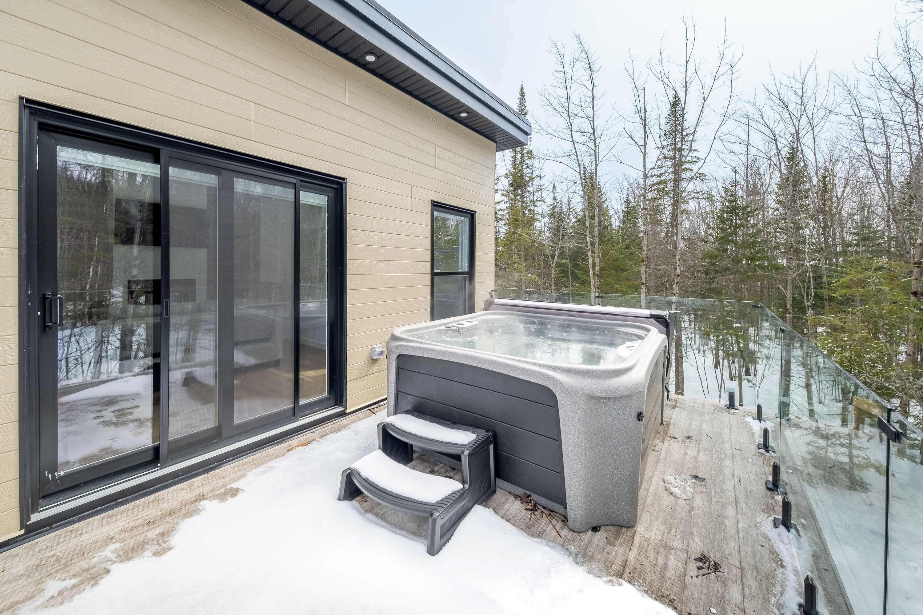 Een modern huis met een glazen deur, een jacuzzi en een houten terras.