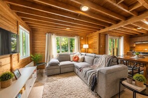 A cozy cabin interior with a sectional sofa, a dining table, and a kitchen area.