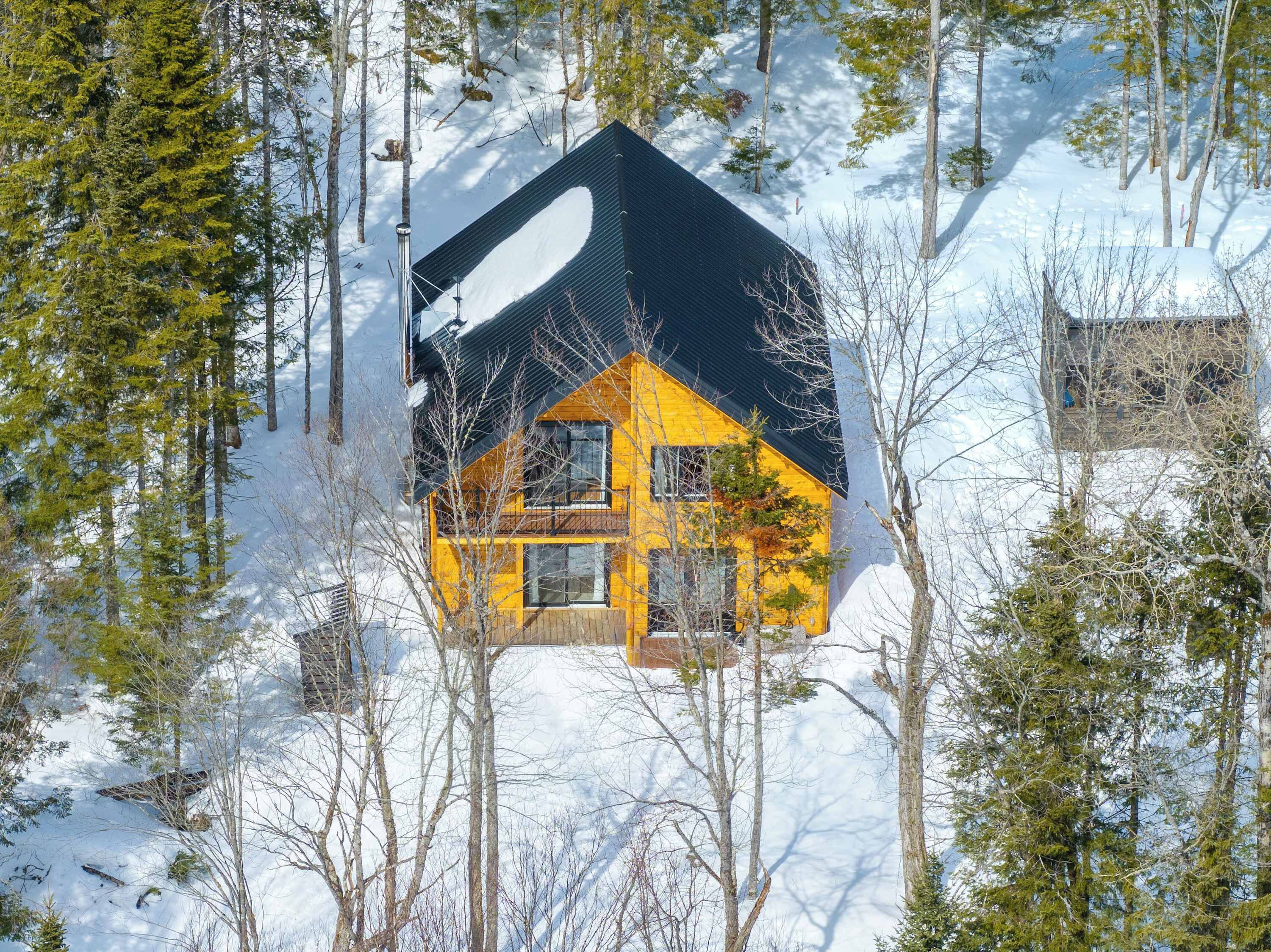 Une cabane dont le toit est recouvert de neige, entourée d’arbres.