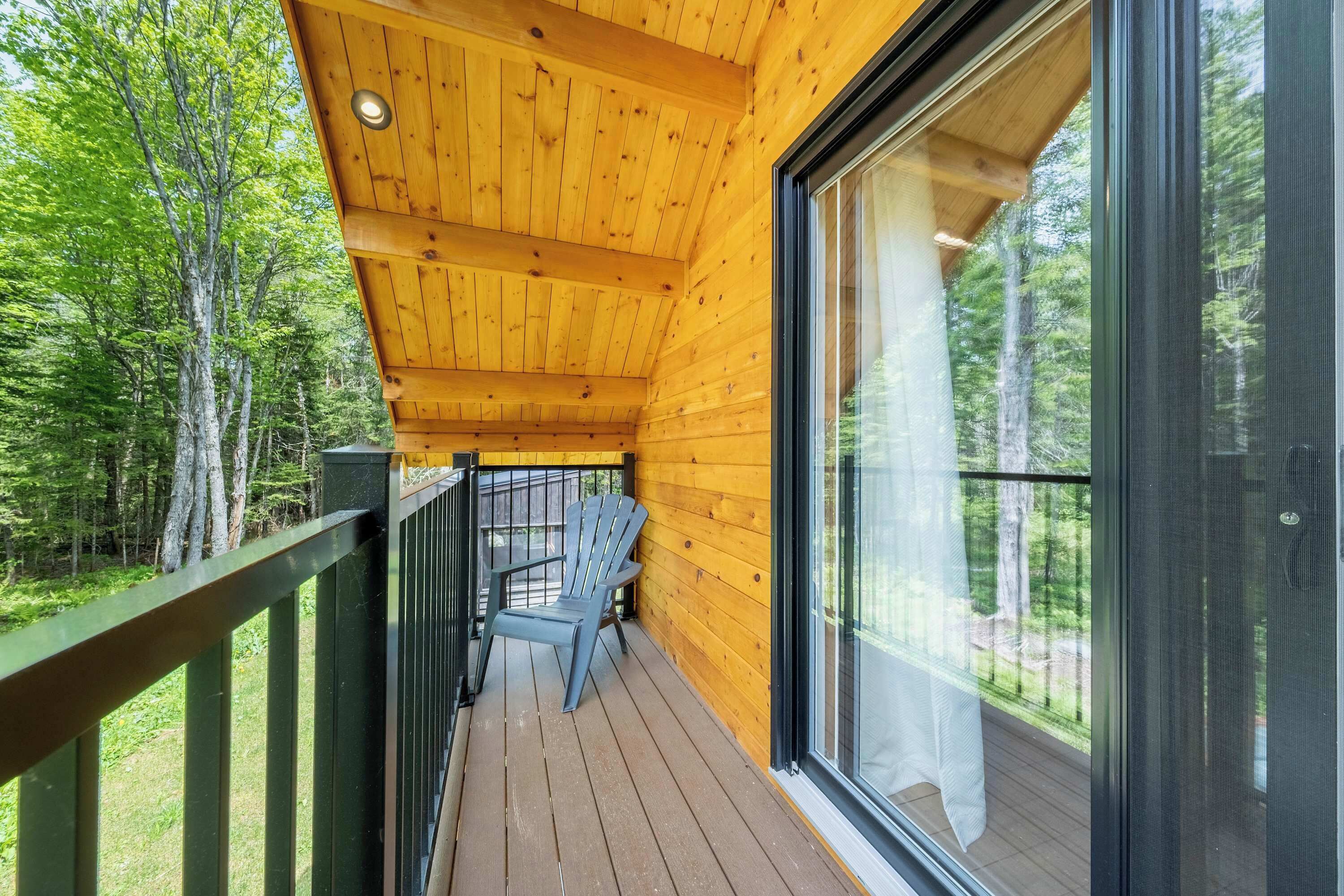 Une terrasse en bois avec une porte vitrée donnant sur une zone boisée.