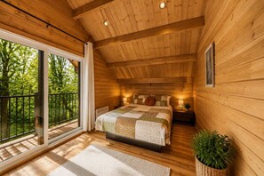 A wooden cabin bedroom with a large bed, a nightstand, a window, and a balcony.