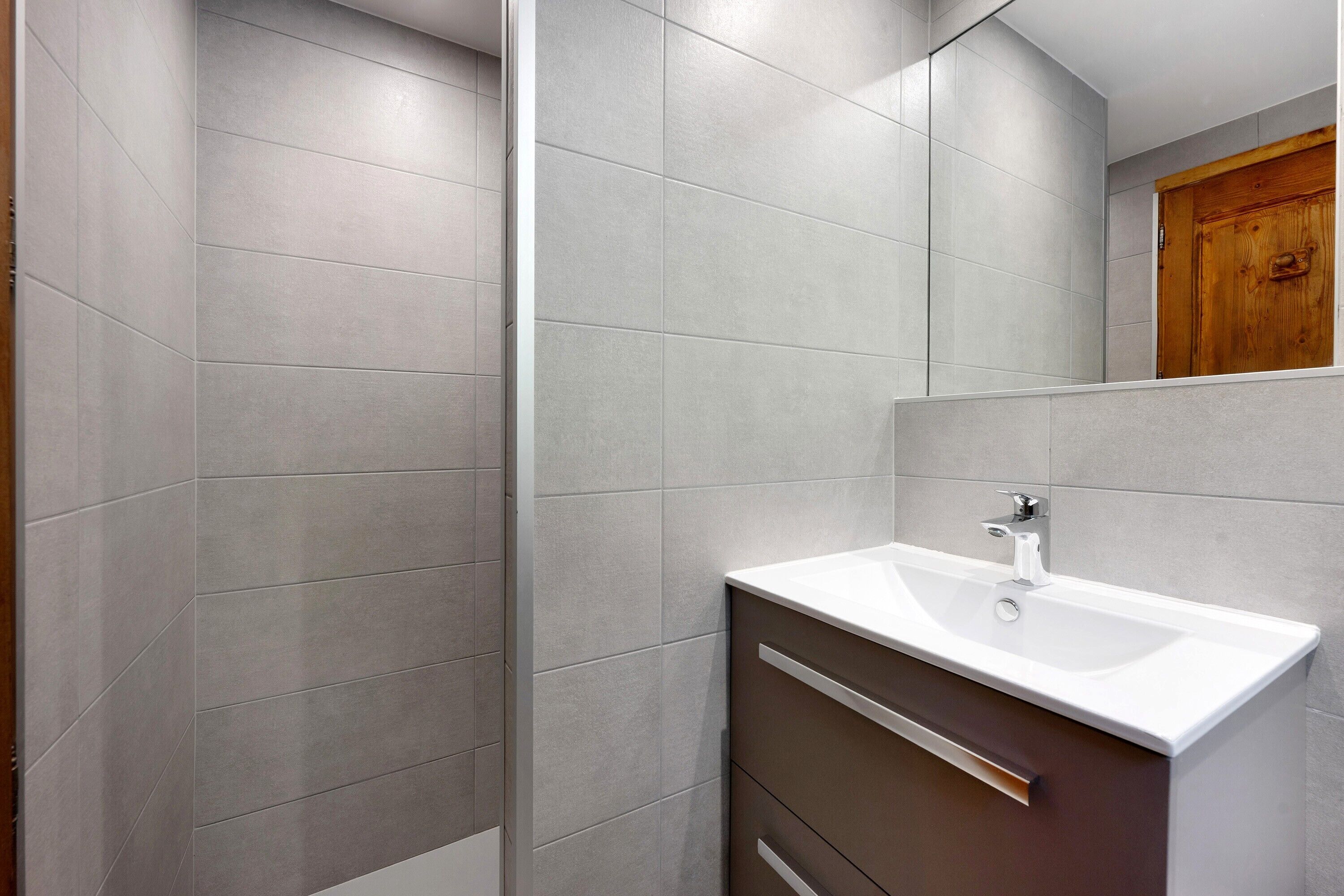 Une salle de bain moderne avec une douche, un lavabo blanc et une porte en bois.
