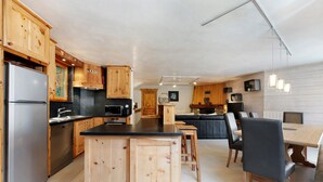 Een moderne keuken met houten kastjes, een roestvrijstalen koelkast en een eethoek met een tafel en stoelen.
