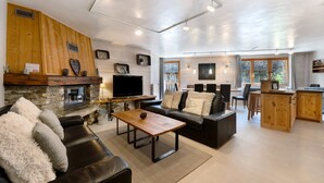 Een moderne woonkamer met een open haard, leren banken, een houten salontafel en een keuken met houten kasten.