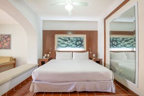 Ein Hotelzimmer mit einem großen Bett, zwei Nachttischen, einer Bank, einem Deckenventilator und Kunstwerken an den Wänden.