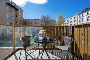 A balcony with a glass partition, two wicker chairs, a small round table, and a vase with flowers. - Comfortable Apartment | View Terrace (Wrocław)