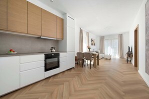 A modern kitchen with white cabinetry, a built-in oven, and a dining area with a table and chairs. - Comfortable Apartment | View Terrace (Wrocław)